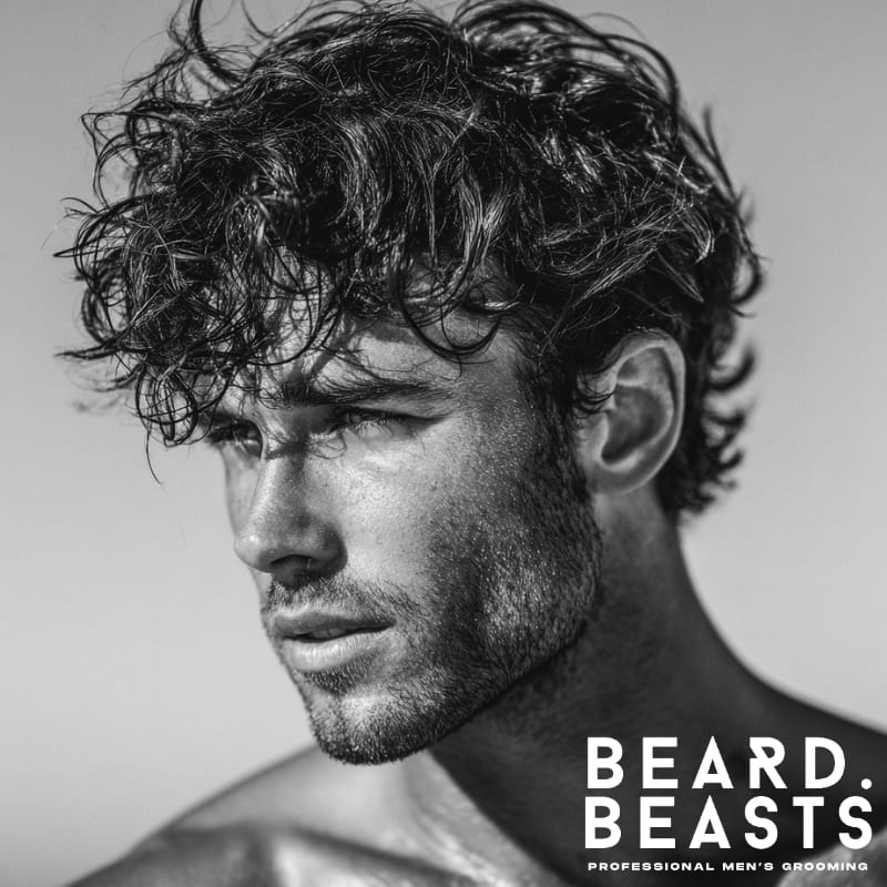 Close-up of a male model with short, messy, dark waves, showcasing a natural and effortless beach-inspired hairstyle.