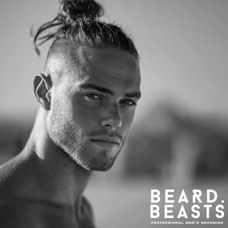 Close-up of a male model with a trendy top knot and faded undercut, showcasing a modern, structured surfer hairstyle.