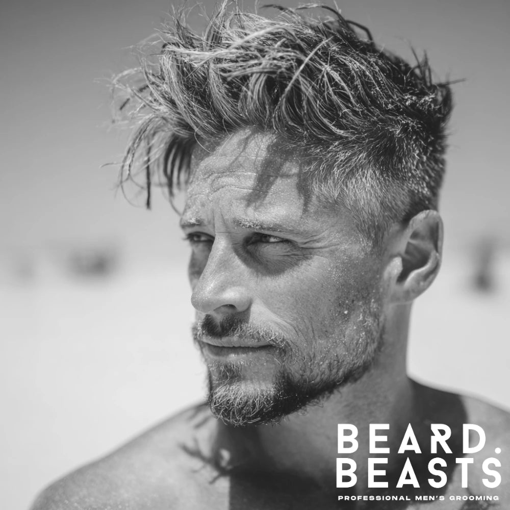 Man with messy faux hawk surfer hairstyle on a sandy beach with windblown texture