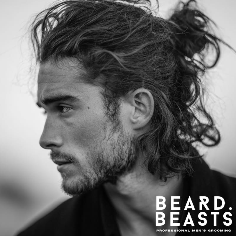 A stylish man with long, textured hair pulled into a messy man bun. The relaxed, untidy strands around the bun create an effortless, casual look, ideal for men seeking a laid-back, trendy hairstyle that combines style and comfort.