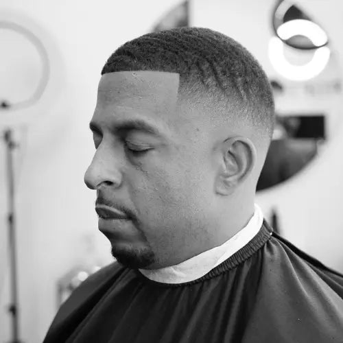 A clean and stylish mid-fade haircut featuring well-defined waves and a sharp lineup. The smooth fade seamlessly transitions from the textured top to the skin, creating a polished and modern look. This classic fade haircut is perfect for men who want a fresh, professional, and well-groomed appearance.