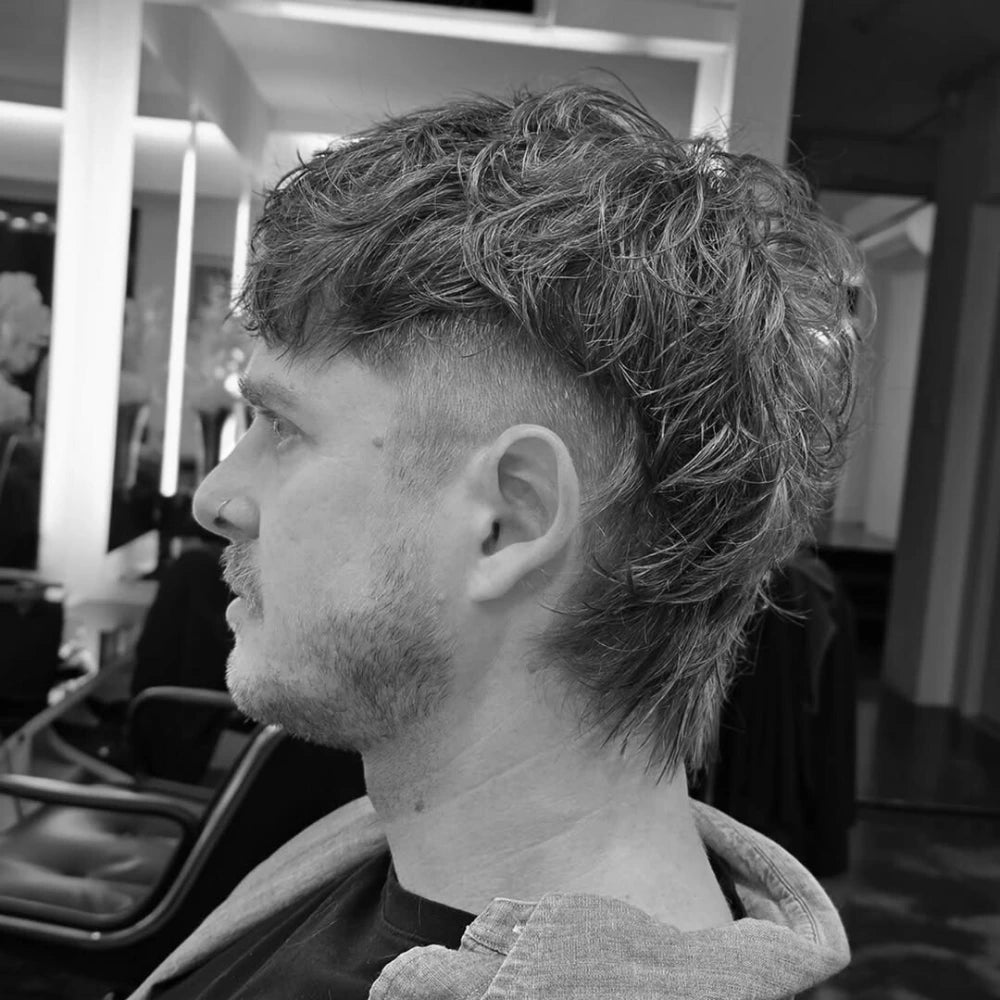 A man with a modern layered mullet haircut. The style features a short, textured top and a longer, layered back.