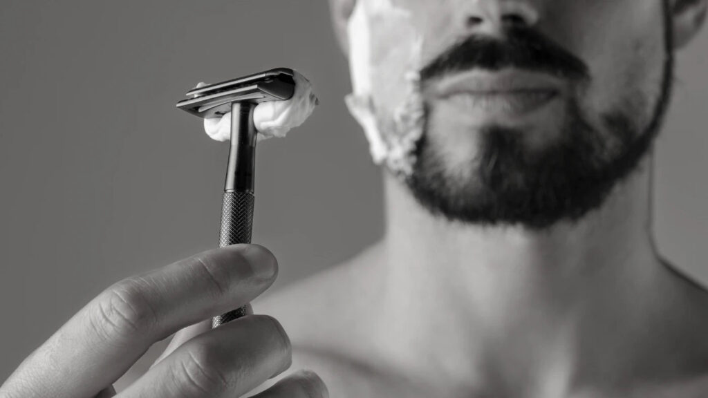 Man holding razor with shaving cream on cheeks, showing recovery process after overworking the beard cheek line