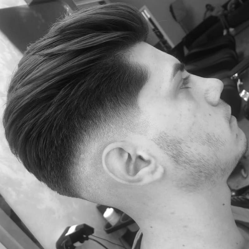 Man with a stylish pompadour drop fade haircut featuring a voluminous, swept-back top and a curved fade line that drops behind the ear for a bold, modern profile.