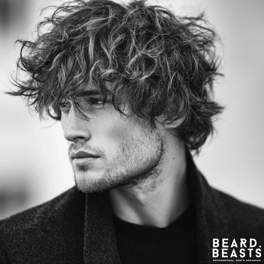 Man with a shaggy layered haircut featuring uneven lengths and textured waves for a rugged, lived-in look.