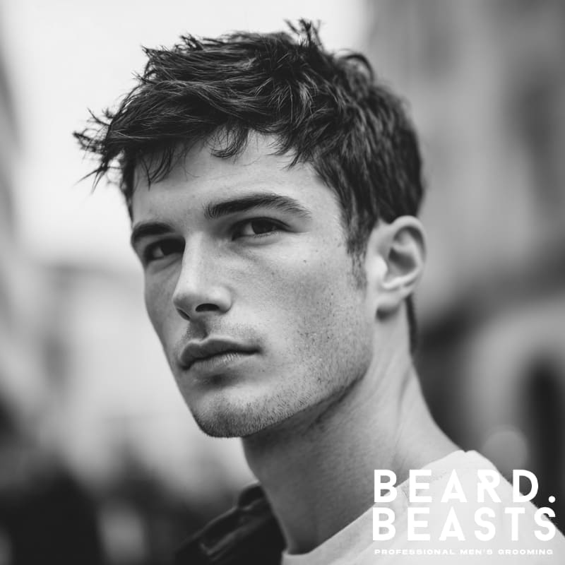 Handsome male model with a short men's flow haircut, styled with natural volume and texture on top, complemented by shorter sides.