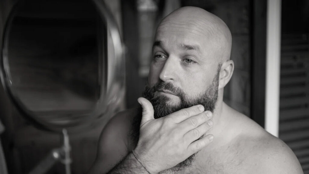 Bald man checking beard symmetry in mirror to avoid uneven trimming mistakes