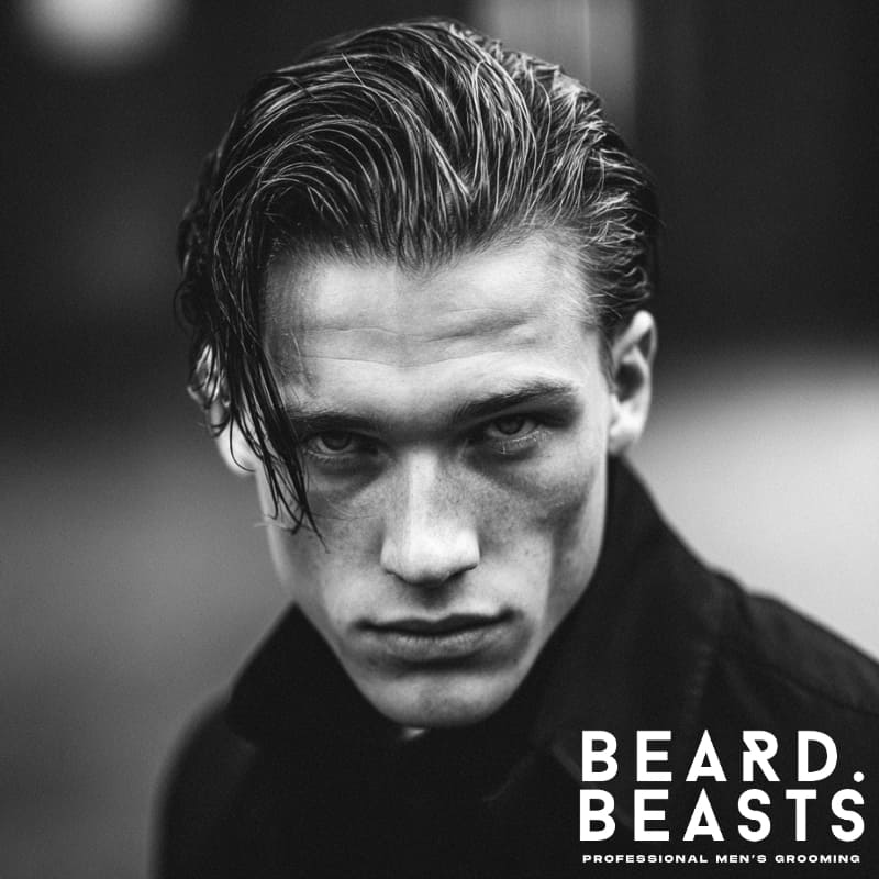 Handsome male model with a slicked-back men's flow haircut, featuring controlled, shiny texture and volume. A sharp, modern take on the classic men's flow hairstyle.