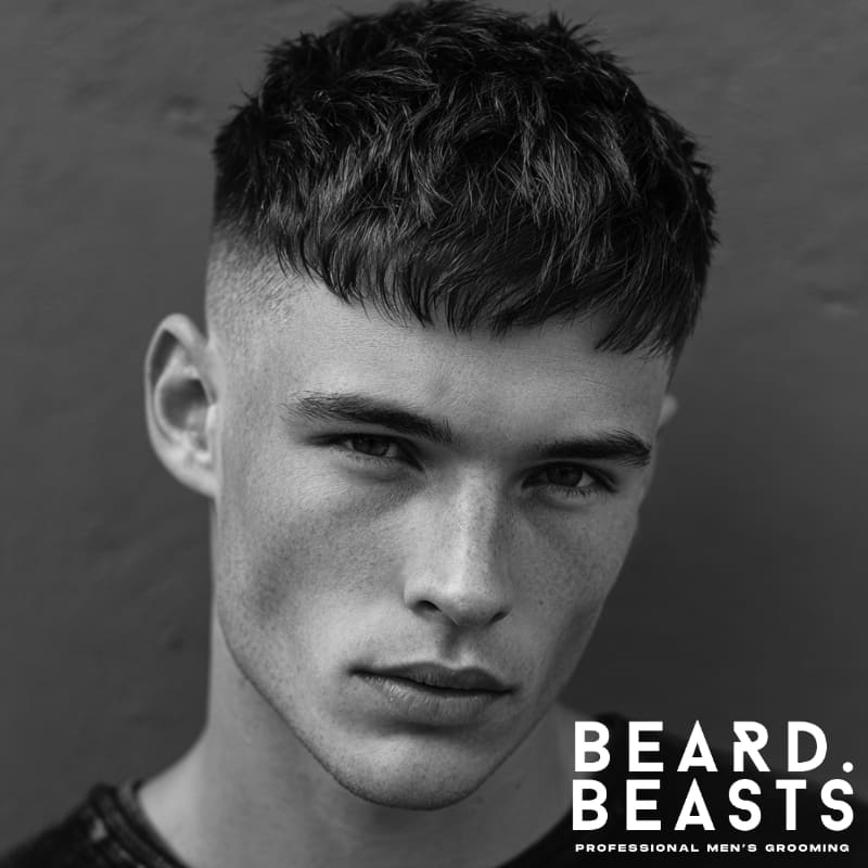 Young man with a textured French crop haircut featuring a blunt fringe, clean fade, and defined choppy layers.