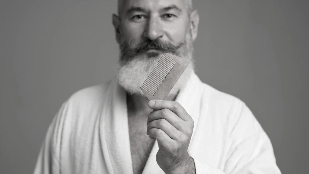 Older man holding a wooden beard comb, showing the importance of combing before trimming to avoid uneven cuts
