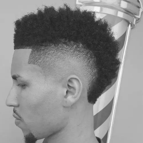 A stylish burst fade haircut for Black men, featuring voluminous, well-defined curls on top with a seamless, skin-blended fade on the sides. The crisp lineup enhances the sharp, modern look, making this fade haircut a trendy choice for those who want a bold yet clean hairstyle.