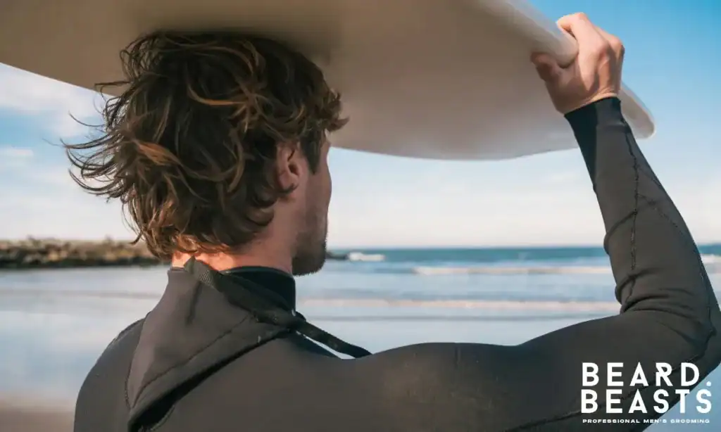 Man with wavy hair holding surfboard on the beach representing sea salt spray texture