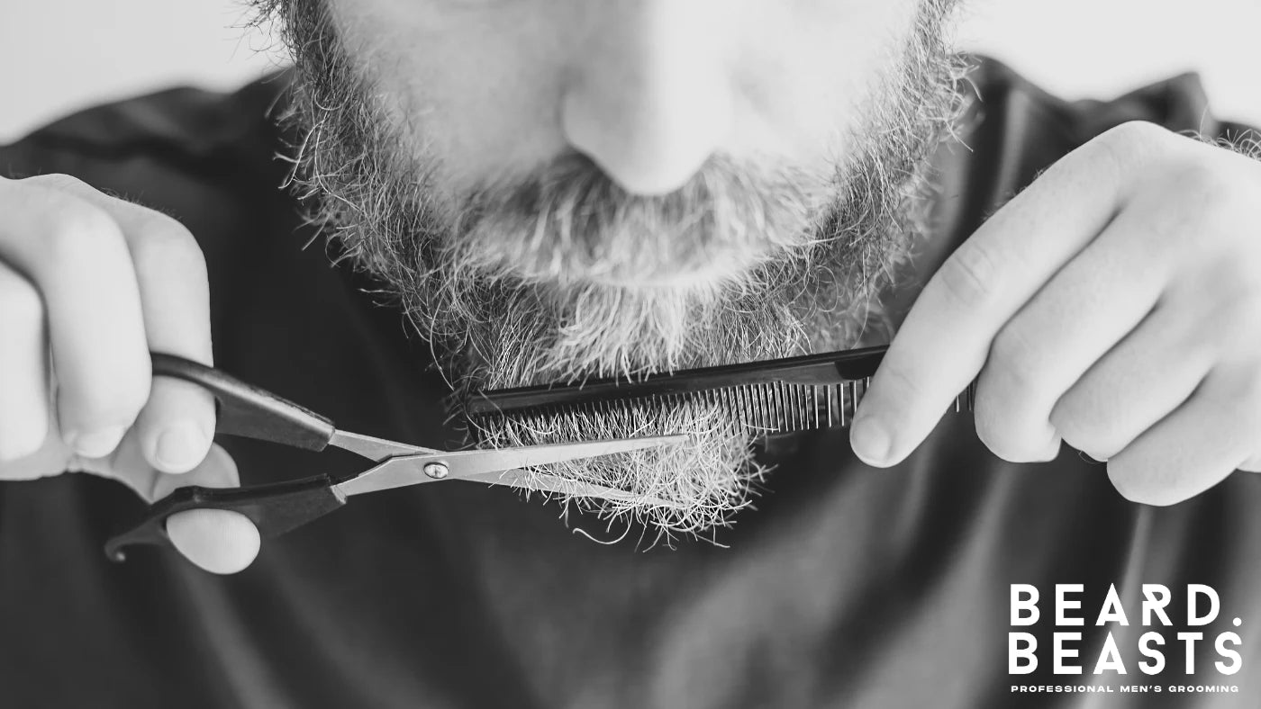 Man trimming his wiry beard with scissors and a comb during a precise grooming session.