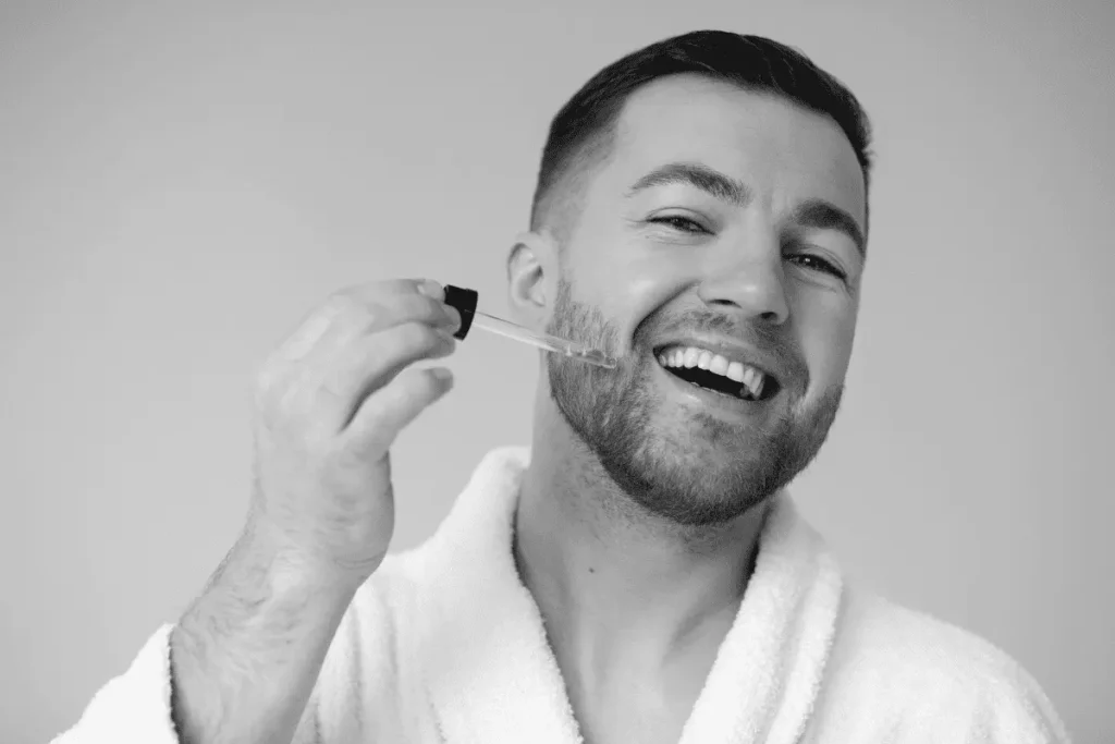 A man applying a lightweight beard oil using a dropper, demonstrating how to use absorbent products to prevent a greasy beard.