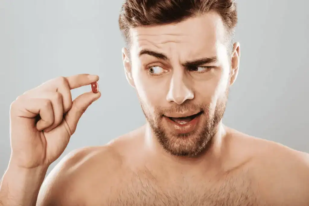 Man holding a supplement capsule and examining it while considering beard growth supplements