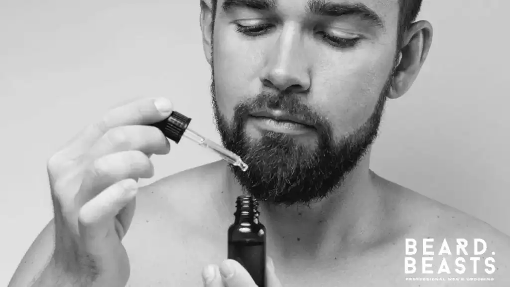 A man with a well-groomed beard applying a vitamin e for beard oil blend using a glass dropper.