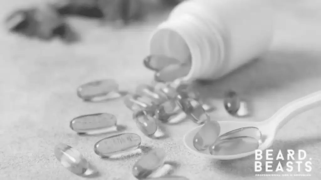 Yellow liquid gel capsules containing vitamin e for beard growth spilled from a white bottle next to a spoon.