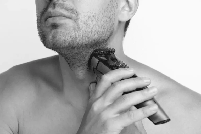 Close-up of man using beard trimmer to shape stubble beard line
