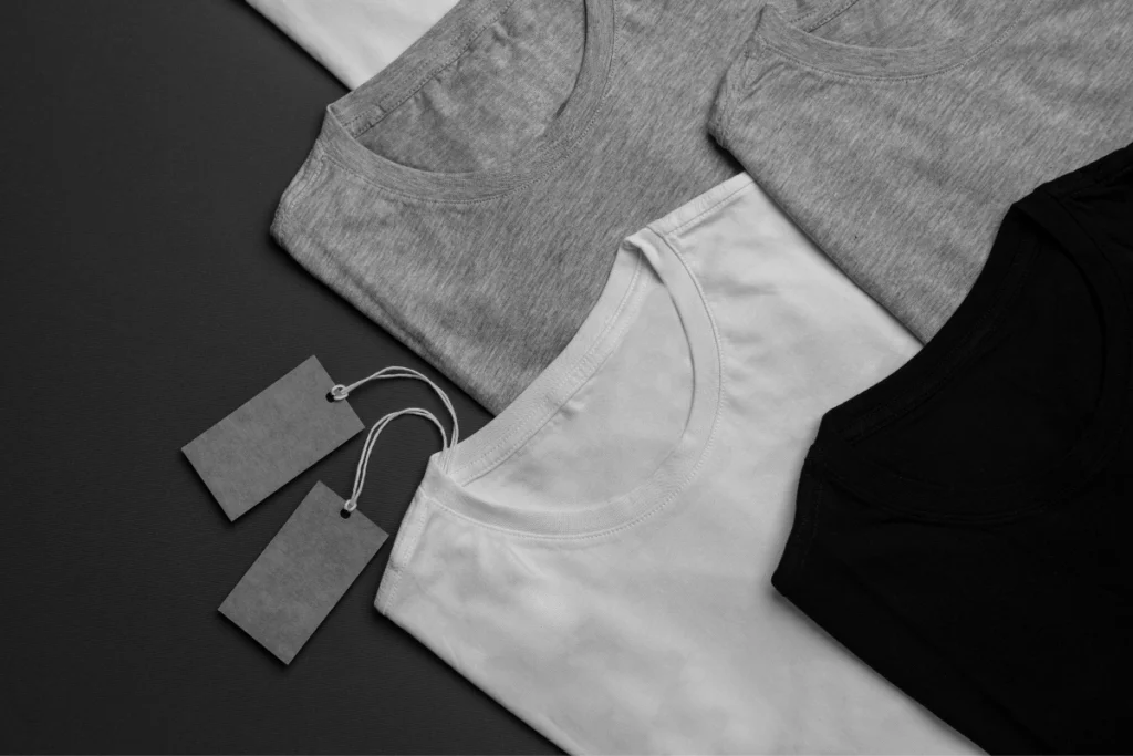 Plain black, white and gray T-shirts with tags, showing simple barbershop merchandise ideas customers are more likely to buy and wear.