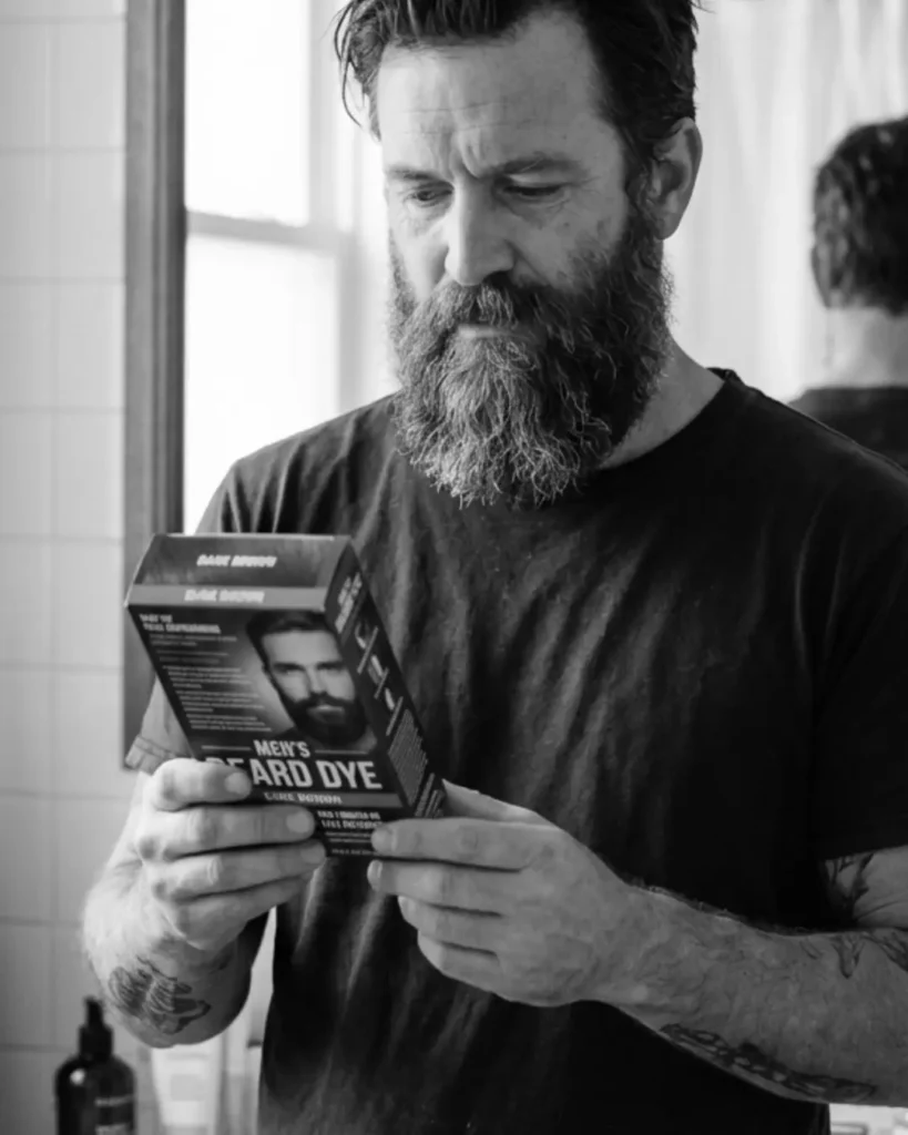 Man with white hairs in his beard holding beard dye, showing why dyeing grey beard hairs too dark can make the beard look unnatural.