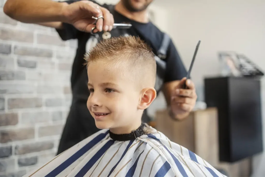 Young boy getting a short haircut at a barbershop while the barber uses scissors.
