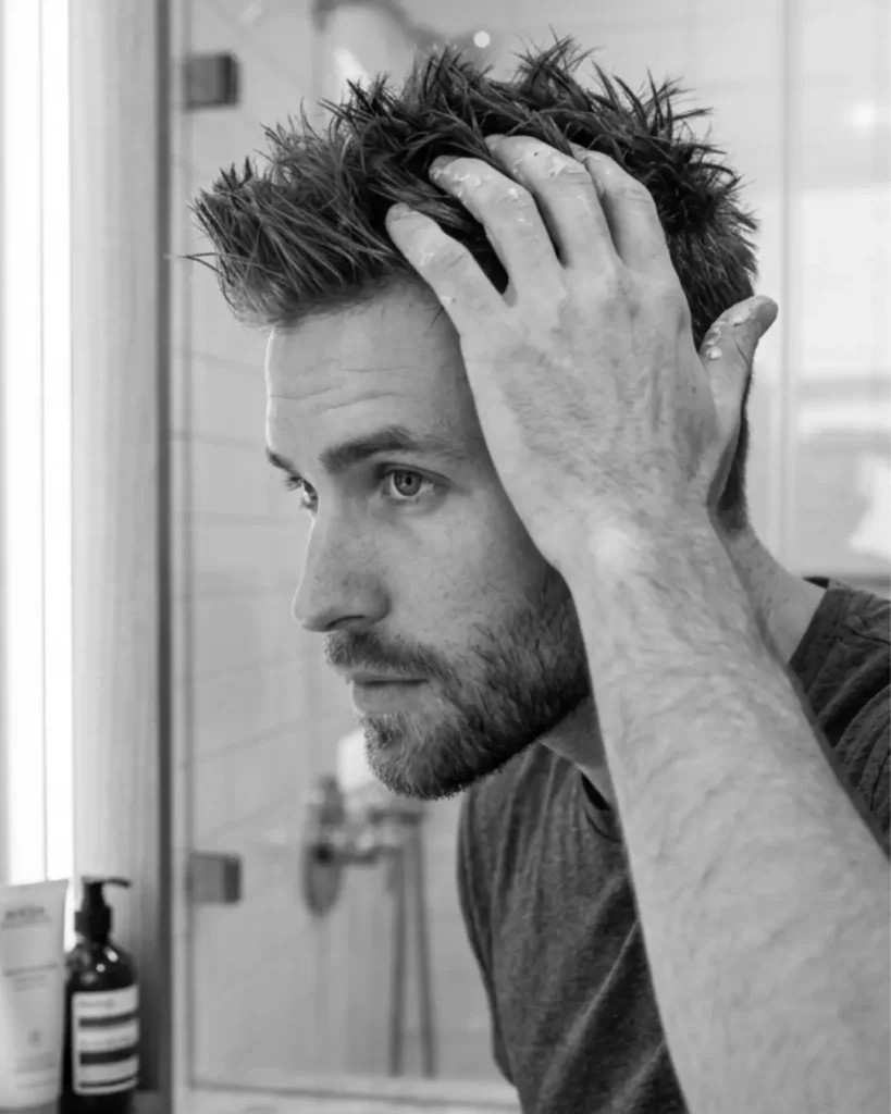 Man styling short textured hair with hair wax, showing how wax adds grip and separation to shorter men’s hairstyles.