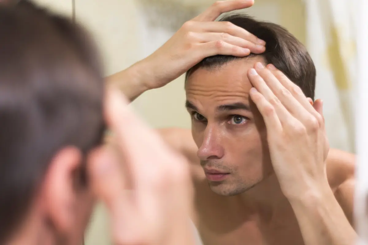 Man checking his thinning hairline in the bathroom mirror while pulling his hair back.