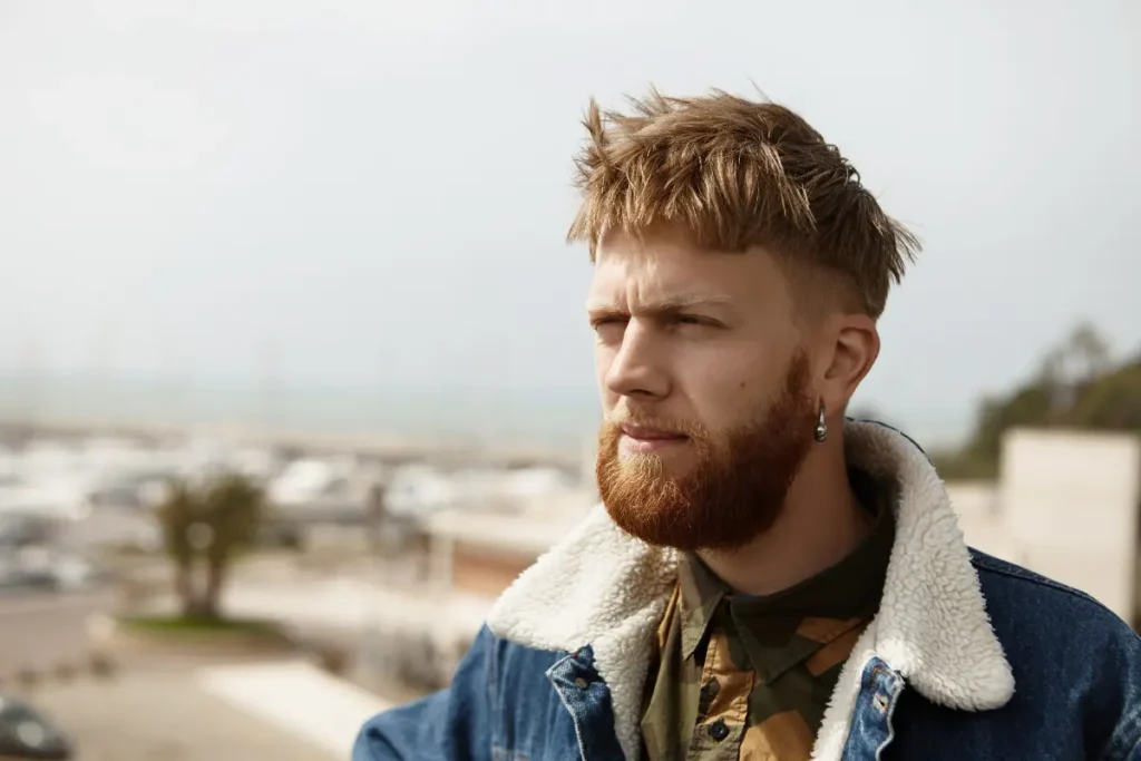 Man with a short textured crop haircut and full beard outdoors.