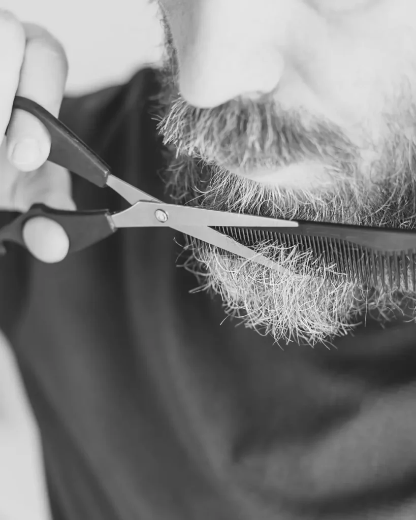 Man trimming his beard with scissors and a comb, showing how removing damaged ends can help manage beard breakage.