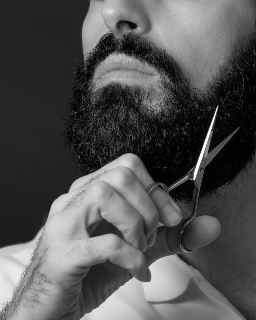 Man trimming a full dark beard with grooming scissors