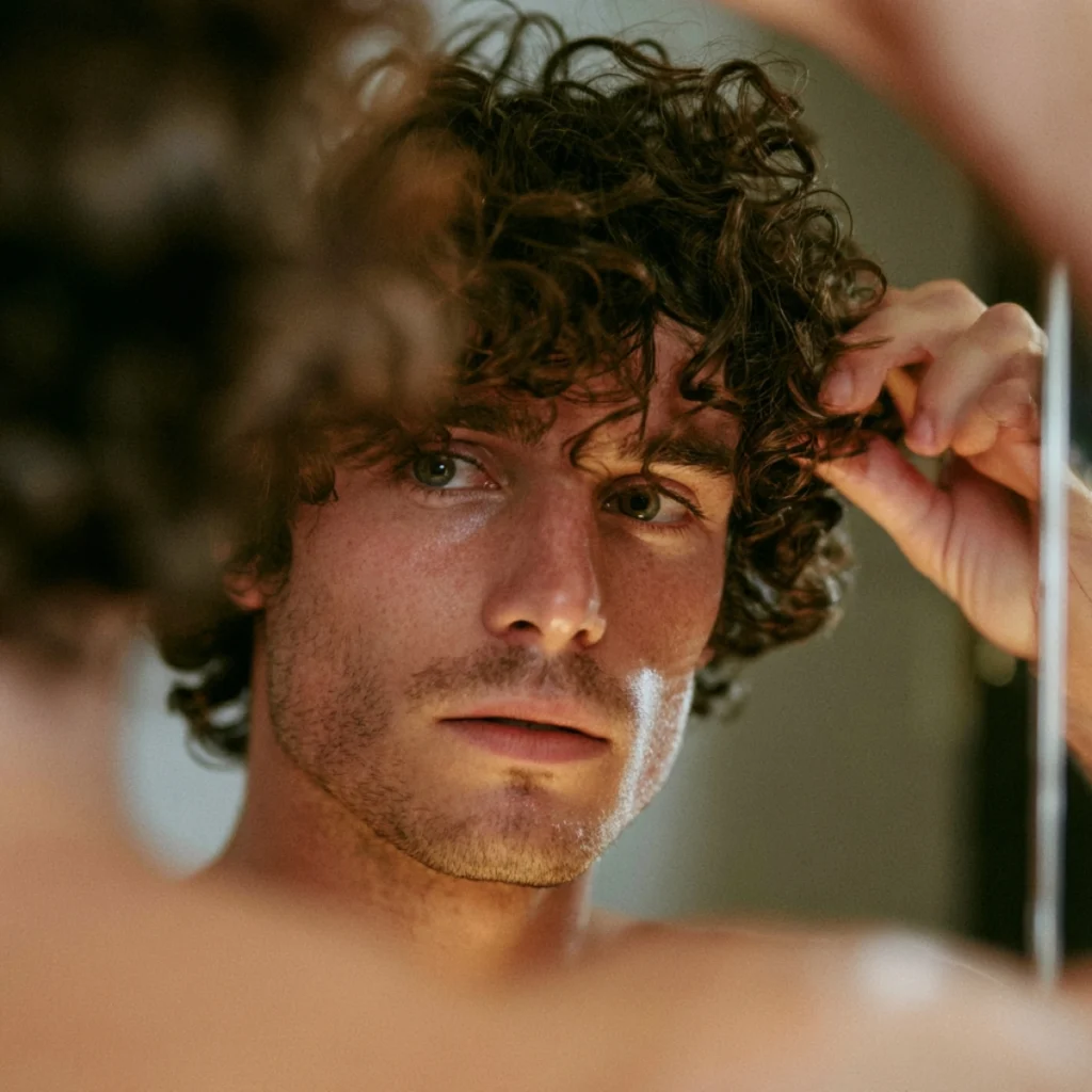 Man checking his curly hair in the mirror as part of a curly hair routine for men.